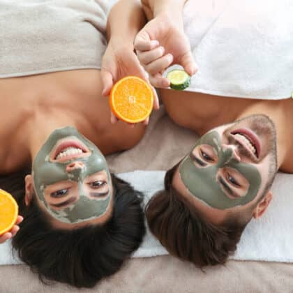 Paar liegend mit Fruchtsäure Maske im Gesicht. Orange und Gurkenscheibe in der Hand